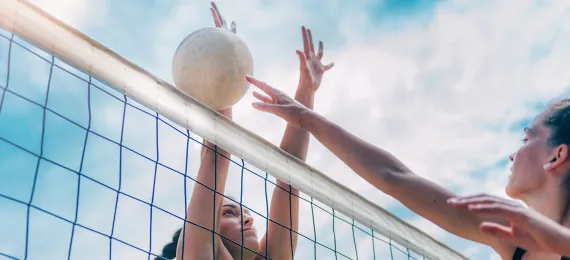 Two girls spiking the volleyball at the net